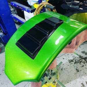 A green car is being painted with black paint.