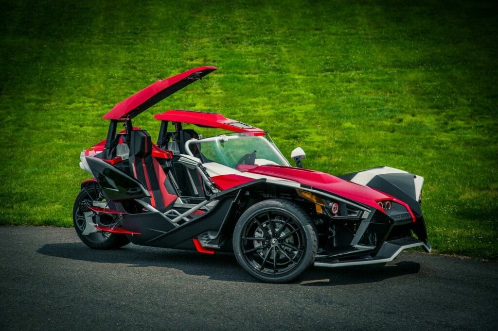 A red and black three wheeled vehicle on the road.