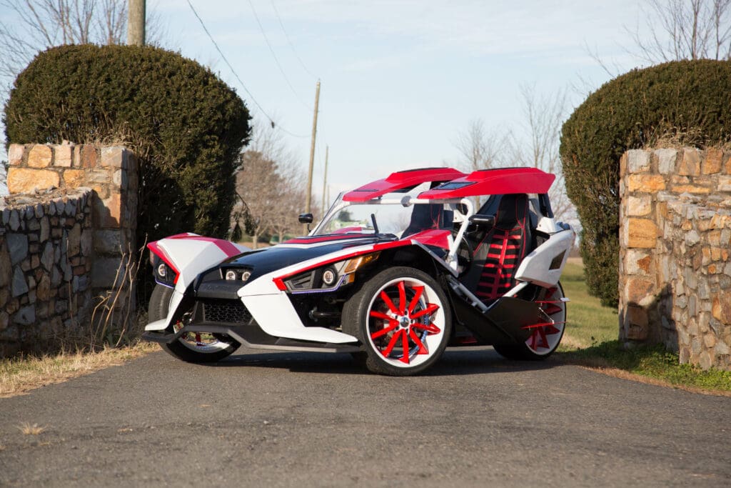 A red and white three wheeled vehicle parked on the side of a road.