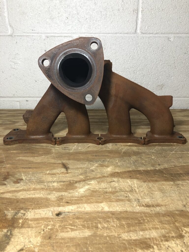 A rusty metal bear shaped exhaust pipe sitting on top of a wooden floor.