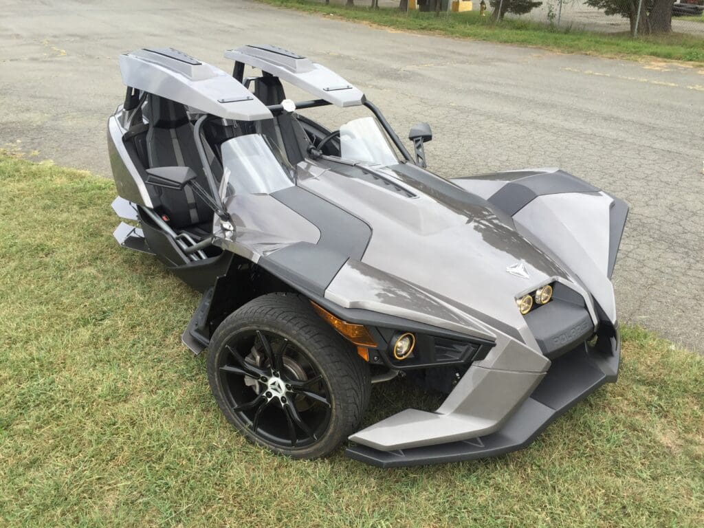 A silver and black three wheeled vehicle parked on the grass.