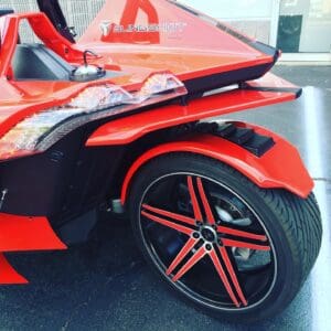 A red and black three wheeled motorcycle parked on the street.
