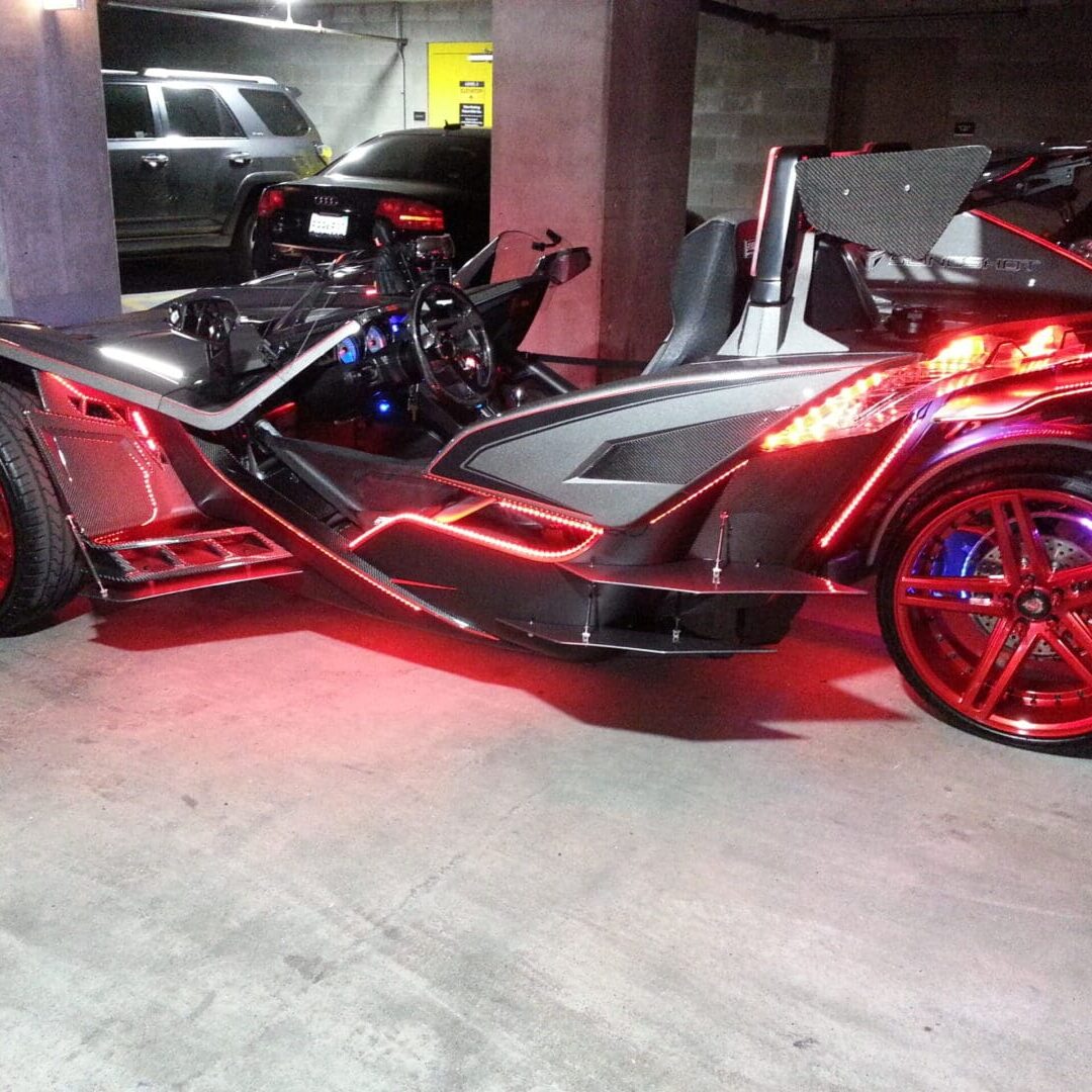 A red and black three wheeled motorcycle parked in a garage.
