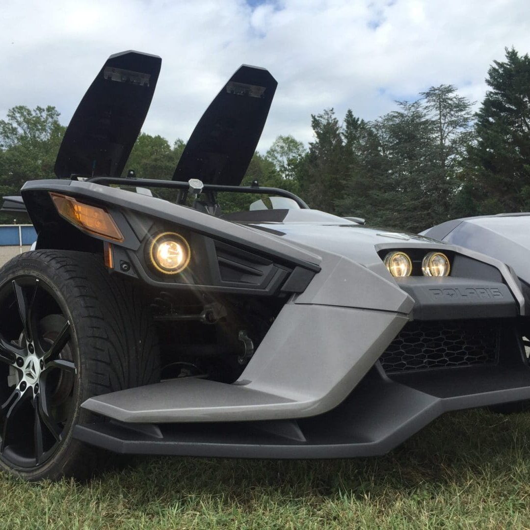 A silver three wheeled vehicle parked in the grass.